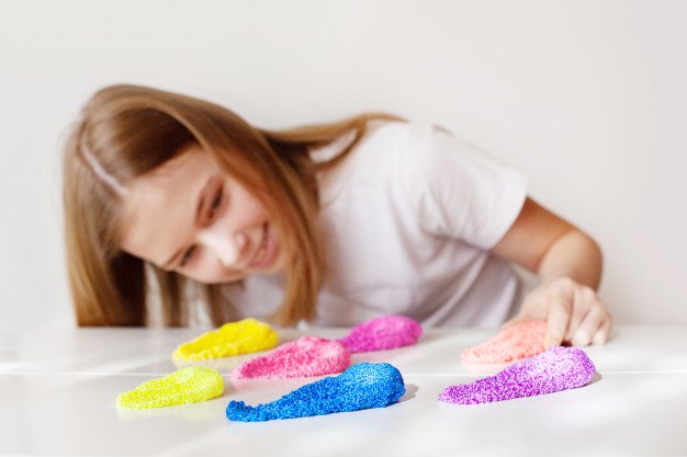 A-girl-smiles-looks-multicolored-slime-lying-table_png_85