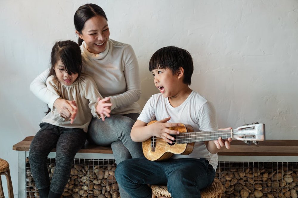 Boy-playing-ukulele-while-sitting-with-mother-and-sister_png_85
