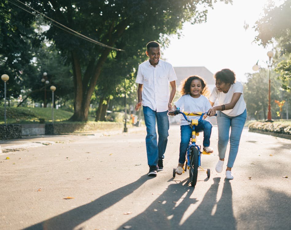 Man-standing-beside-his-wife-teaching-their-child-how-to-ride-bicycle_png_85